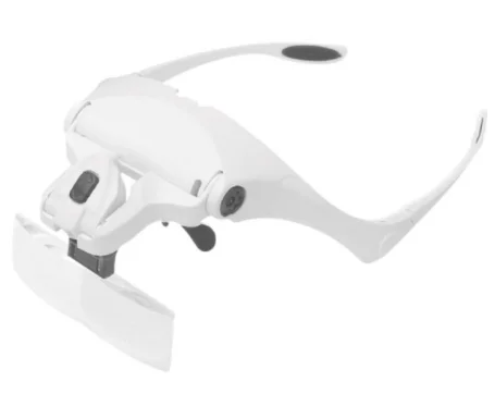 LUPA DE CABEÇA NA COR BRANCA E DETALHES PRETOS, TIPO ÓCULOS, COM LED NA PARTE SUPERIOR DA LUPA E COM FIXAÇÃO DAS LENTES NA PARTE INFERIOR DA LUPA.
