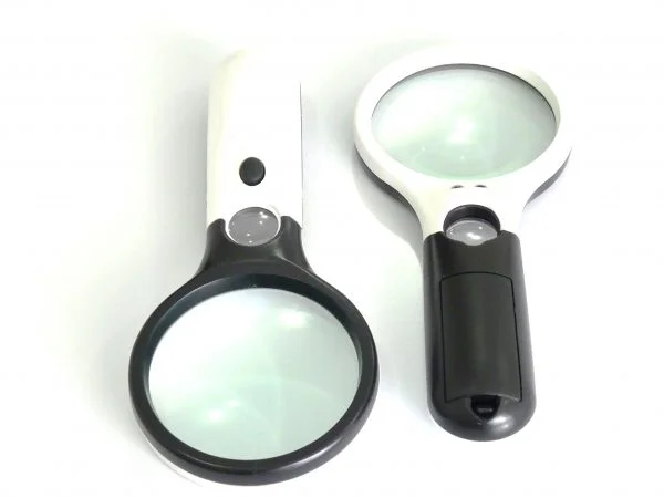 LUPA DE MÃO COM LENTE DE 90MM, NA COR PRETA NO CABO E BRANCA AO REDOR DA LENTE, POSSUI UMA LUPA PEQUENA NO CABO NA PARTE SUPERIOR, POSSUI UM BOTÃO LIGA E DESLIGA NA COR PRETA.