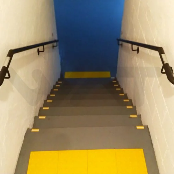 faixa amarela no inicio de uma escada e nos lados próximo à parede, com corrimão e porta azul